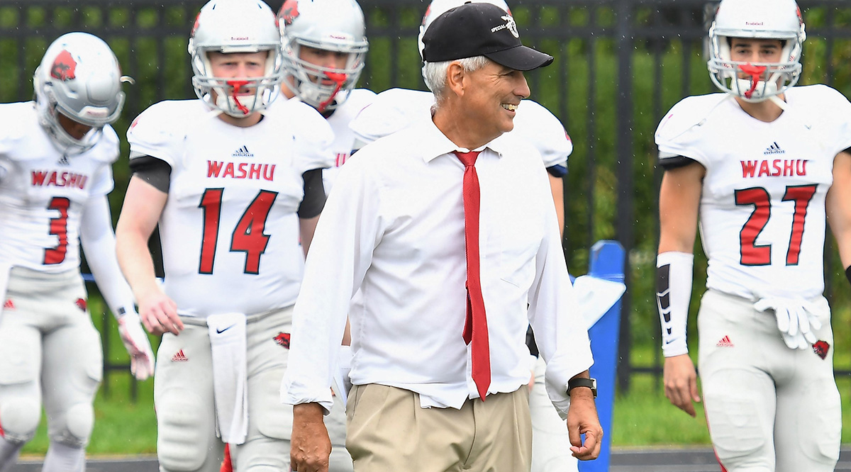 Wash U coach Larry Kindbom, wearing his white shirt and red tie, smiling.